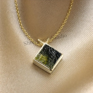 Peut inclure: Un collier en chaîne dorée avec un pendentif carré orné d'une pierre verte et noire.