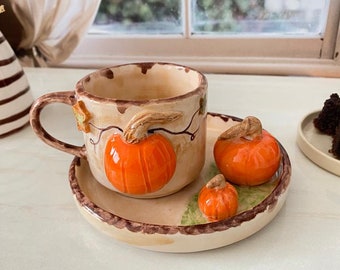 May include: A ceramic coffee cup and saucer set with a pumpkin theme. The cup and saucer are decorated with a brown and orange pumpkin design. The cup has a handle and the saucer has a rim.
