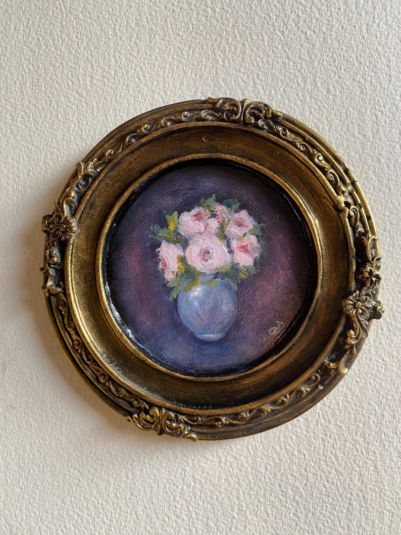 May include: A framed painting of a bouquet of pink flowers in a blue vase. The painting is set against a dark purple background.