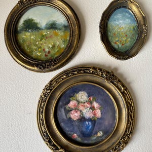 May include: Three framed paintings with gold ornate frames. The paintings depict a field of wildflowers, a field of wildflowers with a blue sky, and a bouquet of pink roses in a blue vase.