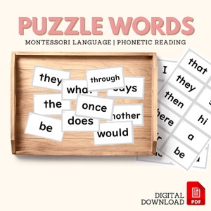 May include: A set of white puzzle word cards with black text, including words like "they", "through", "what", "once", "other", "does", "would", "be", "the", and "says". The cards are arranged in a wooden tray. The words are part of a Montessori language and phonetic reading activity.