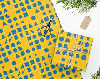 May include: Yellow wrapping paper with a geometric pattern of blue shapes, including circles, squares, and triangles. A wrapped gift box with the same pattern is tied with twine. Black scissors and a blank tag are also present.