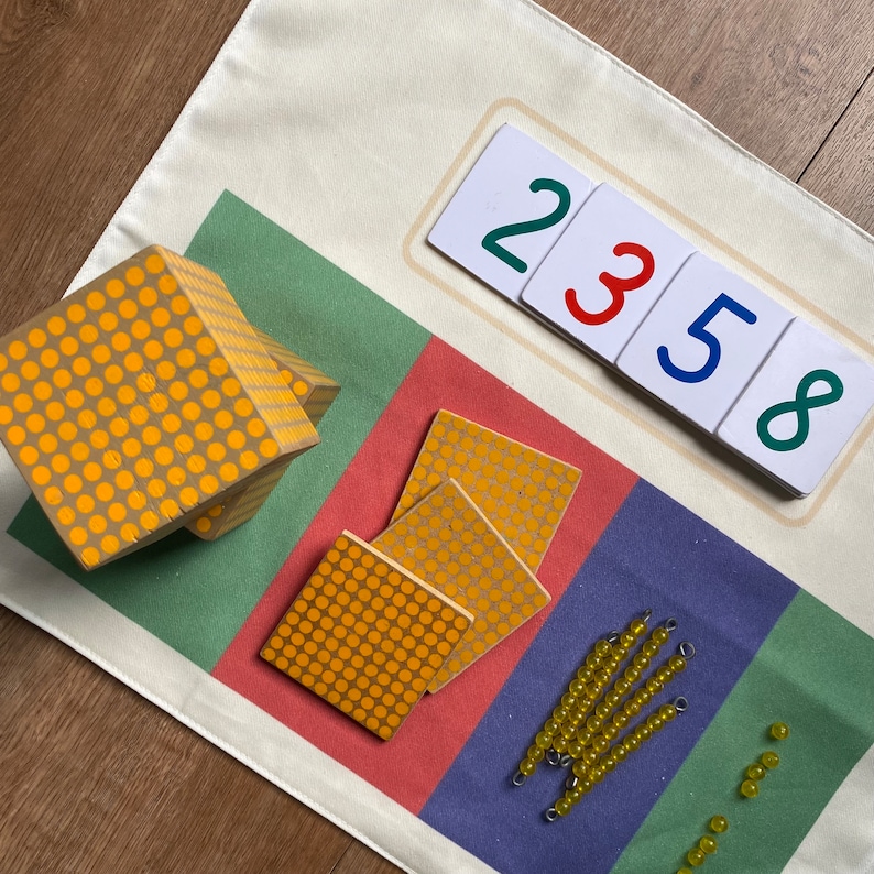 May include: A colorful learning mat with a set of wooden blocks, counting beads, and number cards. The mat features a green, red, blue, and white striped design. The number cards show the numbers 2, 3, 5, and 8.