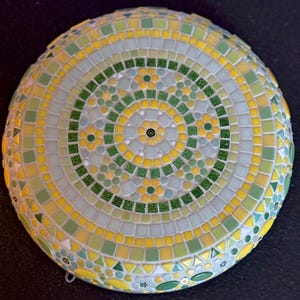 May include: A circular mosaic wall art piece featuring a radial pattern of small square and triangular tiles in shades of yellow, light green, dark green, and white. The design includes concentric rings with floral motifs and glittery accents.