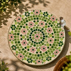 Peut inclure: Un bain d'oiseaux circulaire orné d'un motif en mosaïque composé de carreaux roses, vert clair et vert foncé disposés en motifs floraux et géométriques. Une petite figurine d'oiseau en céramique réaliste est fixée sur le bord du bassin.