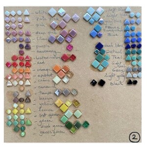 May include: A color chart featuring small, geometric glass tiles arranged in rows by hue, including white, pink, blue, green, and black. Handwritten labels identify each color group, and a number 2 is printed in a circle in the bottom right corner.