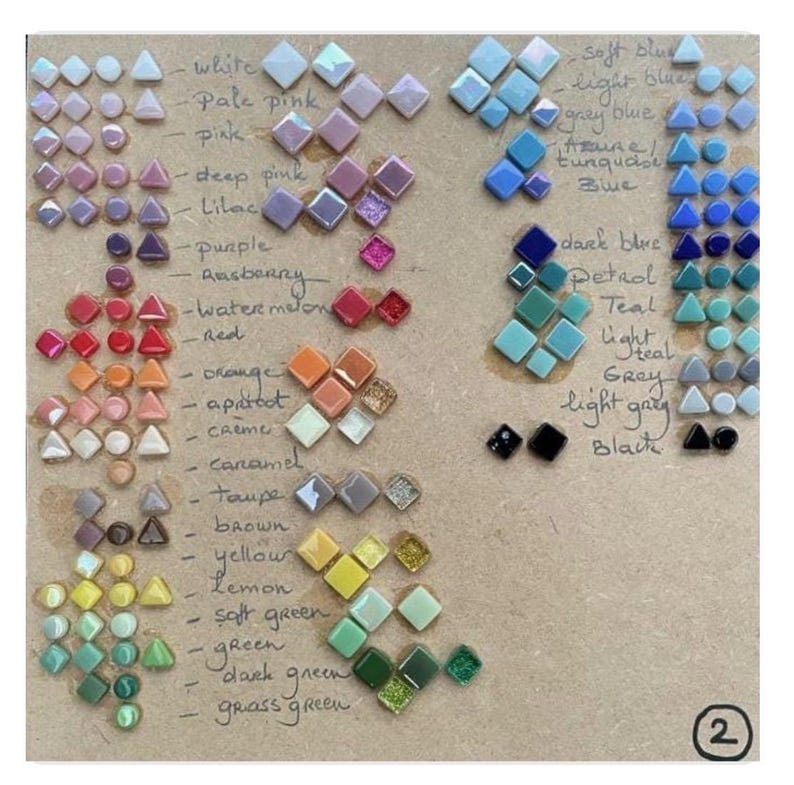 May include: A color chart featuring small, geometric glass tiles arranged in rows by hue, including white, pink, blue, green, and black. Handwritten labels identify each color group, and a number 2 is printed in a circle in the bottom right corner.