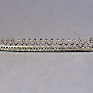 May include: Silver-toned metal trim with a decorative design featuring a repeating pattern of small, rounded points and a scalloped edge.