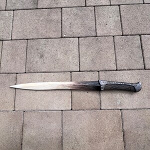 May include: A long, silver-colored sword with a brown handle. The sword has a slightly curved blade and intricate details on the handle.
