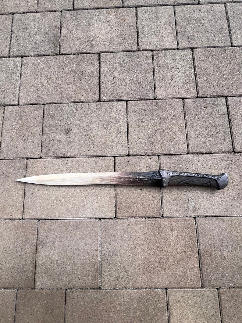 May include: A long, silver-colored sword with a brown handle. The sword has a slightly curved blade and intricate details on the handle.