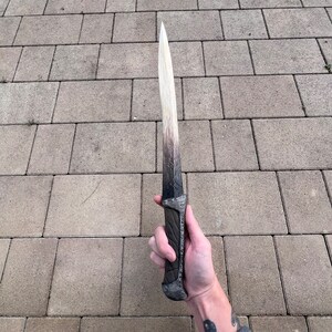 May include: A white and black dagger with a silver handle. The blade is long and thin, and the handle is decorated with intricate designs.