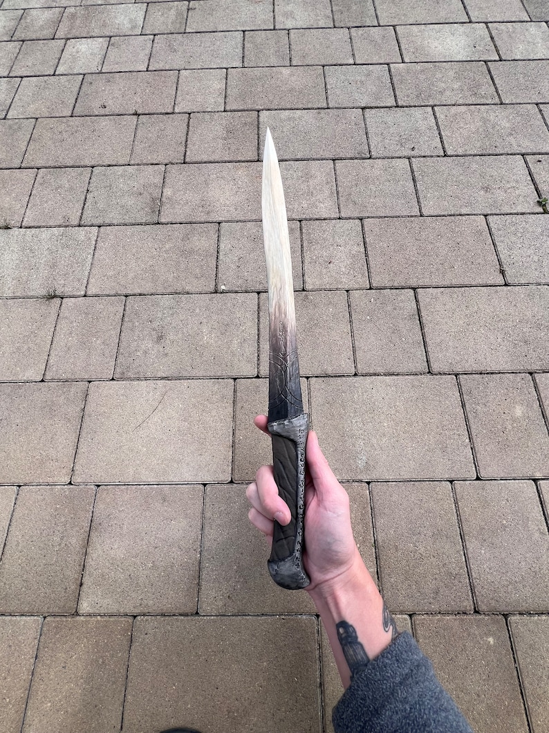 May include: A white and black dagger with a silver handle. The blade is long and thin, and the handle is decorated with intricate designs.