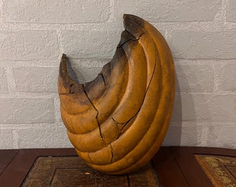 Puede incluir: Objeto decorativo tallado en forma de media luna. La pieza es de un color marrón dorado cálido con zonas más oscuras y carbonizadas. La superficie tiene un patrón texturizado y acanalado, y el objeto parece ser de madera.