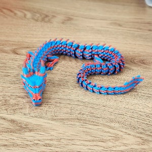 Puede incluir: Una figurita de drag&oacute;n azul y rojo con un cuerpo segmentado y una cabeza detallada. El drag&oacute;n est&aacute; enroscado en un c&iacute;rculo.
