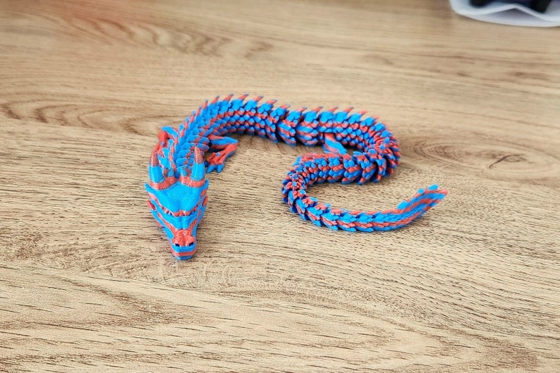 Puede incluir: Una figurita de drag&oacute;n azul y rojo con un cuerpo segmentado y una cabeza detallada. El drag&oacute;n est&aacute; enroscado en un c&iacute;rculo.