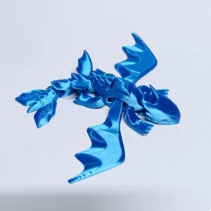 May include: A blue 3D printed dragon figurine with articulated wings and tail. The dragon is posed in flight with its wings spread wide.
