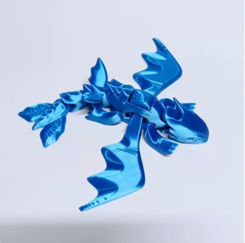 May include: A blue 3D printed dragon figurine with articulated wings and tail. The dragon is posed in flight with its wings spread wide.