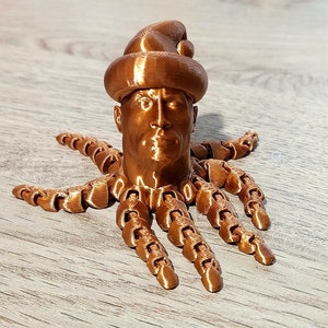 Puede incluir: Una figurita impresa en 3D de una persona con un gorro de Pap&aacute; Noel y un cuerpo de pulpo. La figurita est&aacute; hecha de un material de color cobre.
