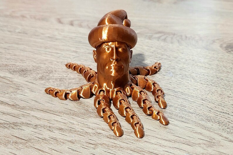 Puede incluir: Una figurita impresa en 3D de una persona con un gorro de Pap&aacute; Noel y un cuerpo de pulpo. La figurita est&aacute; hecha de un material de color cobre.