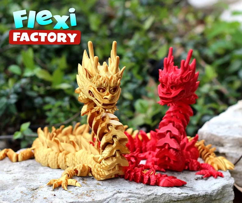 May include: Two articulated dragon figurines, one gold and one red, posed on a rock. The dragons are made of plastic and have a segmented body. The text "Flexi Factory" is visible in the background.