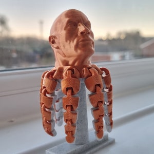 Op de afbeelding: Een 3D-geprint buste van een mannenhoofd met een koperen afwerking. De buste is gemonteerd op een basis met meerdere scharnierende armen.