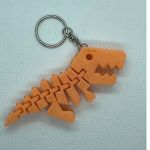 Puede incluir: Un llavero de pl&aacute;stico de esqueleto de dinosaurio de color melocot&oacute;n con un anillo y una cadena de metal plateado.