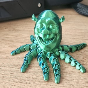 Puede incluir: Una figura verde impresa en 3D de Shrek, el ogro de la pel&iacute;cula Shrek, con una cara sonriente y ocho tent&aacute;culos.