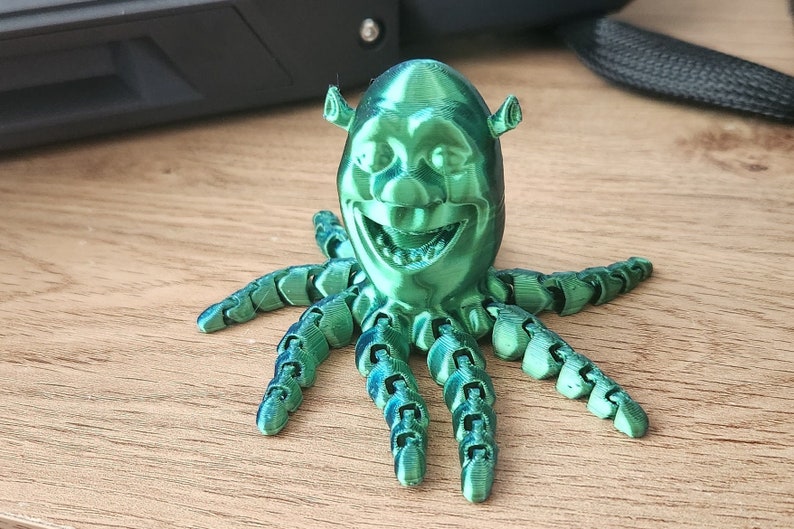 Puede incluir: Una figura verde impresa en 3D de Shrek, el ogro de la pel&iacute;cula Shrek, con una cara sonriente y ocho tent&aacute;culos.