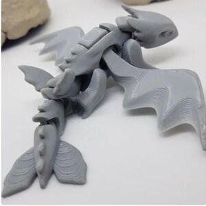 May include: A gray 3D printed dragon figurine with articulated wings and tail. The dragon has a detailed, textured surface.