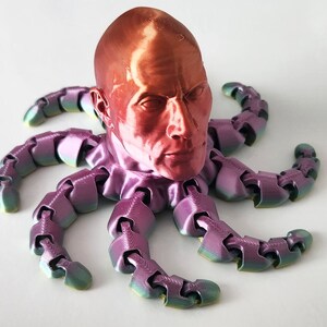 May include: A 3D printed sculpture of a human head with a metallic red finish, mounted on a multi-colored octopus with eight tentacles.