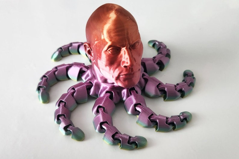 May include: A 3D printed sculpture of a human head with a metallic red finish, mounted on a multi-colored octopus with eight tentacles.