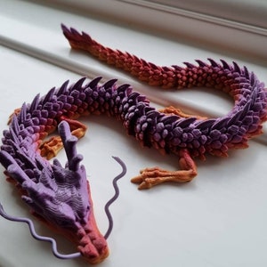 May include: A 3D printed dragon figurine with a purple and orange gradient color scheme. The dragon is curled up with its head resting on its tail.