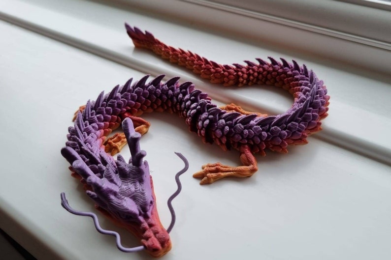 May include: A 3D printed dragon figurine with a purple and orange gradient color scheme. The dragon is curled up with its head resting on its tail.