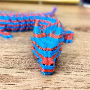 Puede incluir: Una figurita de drag&oacute;n rayada de azul y rojo con una cabeza detallada y un cuerpo largo y segmentado.