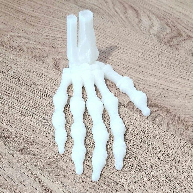 May include: A white plastic model of a human hand skeleton. The hand is posed with the fingers spread out.
