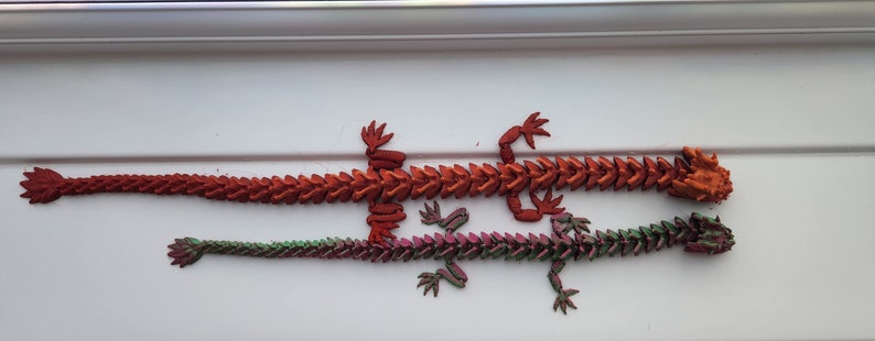 May include: Two 3D printed articulated dragon figurines. The larger dragon is red and the smaller dragon is green and purple.
