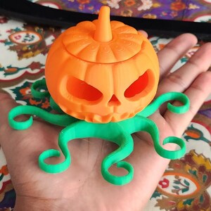 May include: A 3D printed orange pumpkin with a green octopus base. The pumpkin has a carved face and a stem on top.
