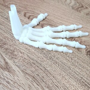May include: A white plastic model of a human hand skeleton. The hand is open and the fingers are spread out.