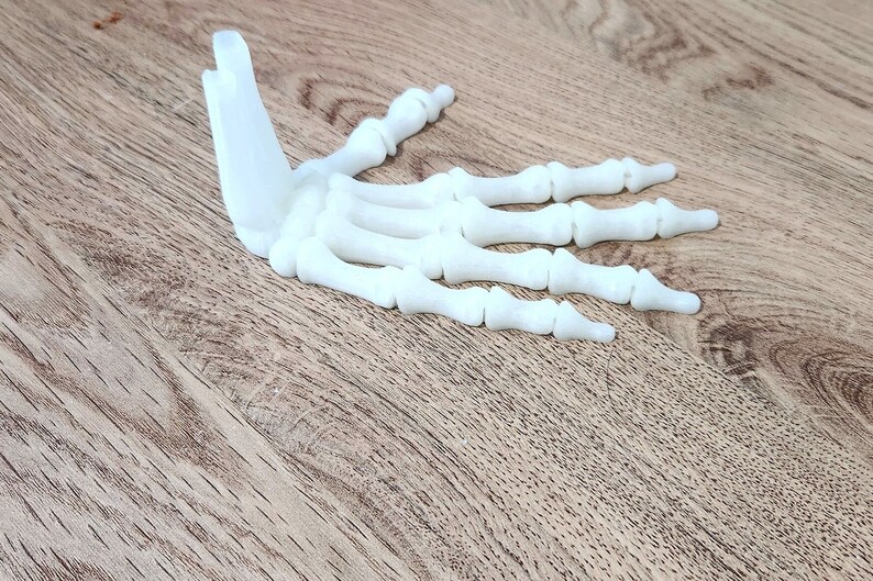 May include: A white plastic model of a human hand skeleton. The hand is open and the fingers are spread out.