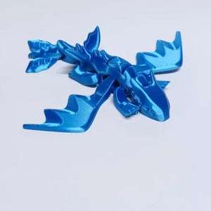 May include: A blue 3D printed dragon figurine with wings outstretched. The dragon has a detailed textured surface and a slightly open mouth.