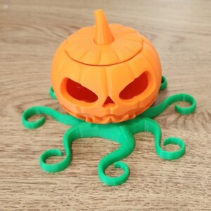 May include: A 3D printed orange pumpkin with a green octopus base. The pumpkin has a carved face and a removable lid.