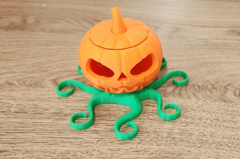 May include: A 3D printed orange pumpkin with a green octopus base. The pumpkin has a carved face and a removable lid.