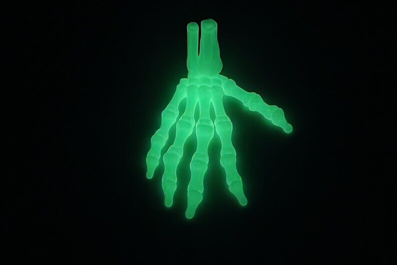 May include: A glowing green skeleton hand with five fingers. The hand is made of plastic and is a Halloween decoration.
