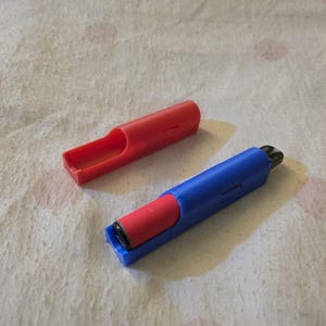 K&ouml;nnte beinhalten: Zwei stiftartige Kunststoffobjekte. Eines ist rot und offen, das andere blau mit einem roten Einsatz und einer schwarzen Spitze. Die Objekte liegen auf einer wei&szlig;en, strukturierten Oberfl&auml;che mit rosa Flecken.