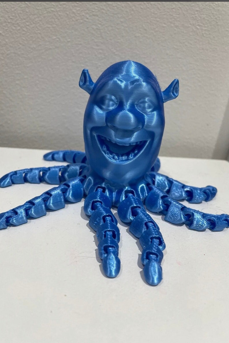 Puede incluir: Una figura azul de Shrek como pulpo impresa en 3D. La figura tiene una cara detallada y ocho tent&aacute;culos.