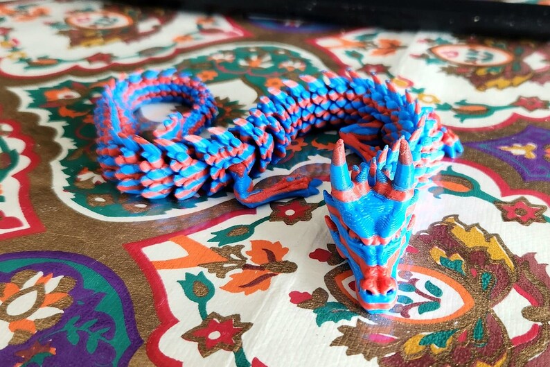 Puede incluir: Una figurita de drag&oacute;n impresa en 3D azul y roja con una espalda espinosa y una cara detallada.