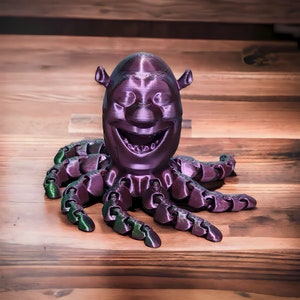 Puede incluir: Un pulpo de color morado impreso en 3D con una cara sonriente. El pulpo tiene ocho tent&aacute;culos y est&aacute; hecho de un material liso y brillante.