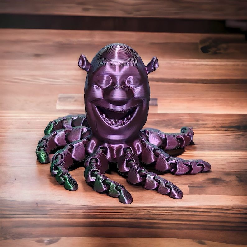 Puede incluir: Un pulpo de color morado impreso en 3D con una cara sonriente. El pulpo tiene ocho tent&aacute;culos y est&aacute; hecho de un material liso y brillante.