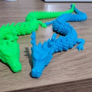 May include: Three 3D printed dragon figurines. One is green, one is blue, and one is a lighter shade of blue.