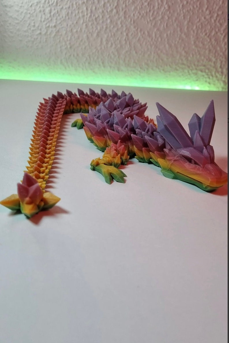 May include: A 3D printed rainbow colored lizard with a spiky, crystal-like texture. The lizard is posed with its tail curled up and its head raised.